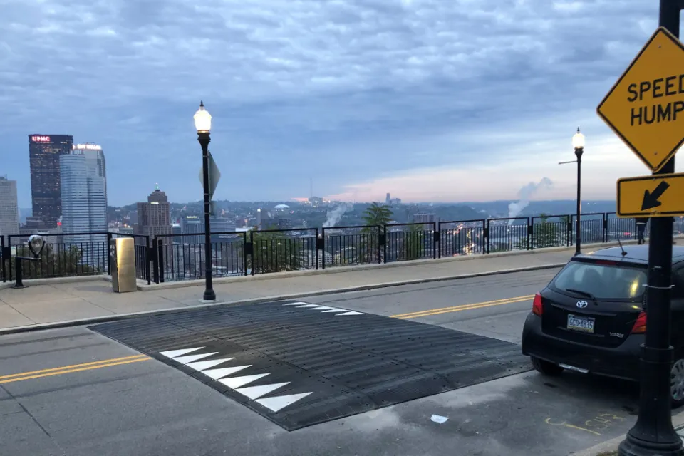 Wide speed hump on Pittsburgh bridge with yellow Speed Hump sign on sidewalk.